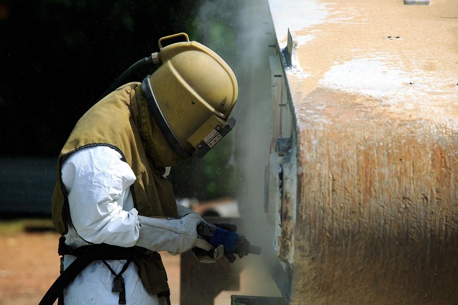 Worker is removing paint by air pressure sand blasting